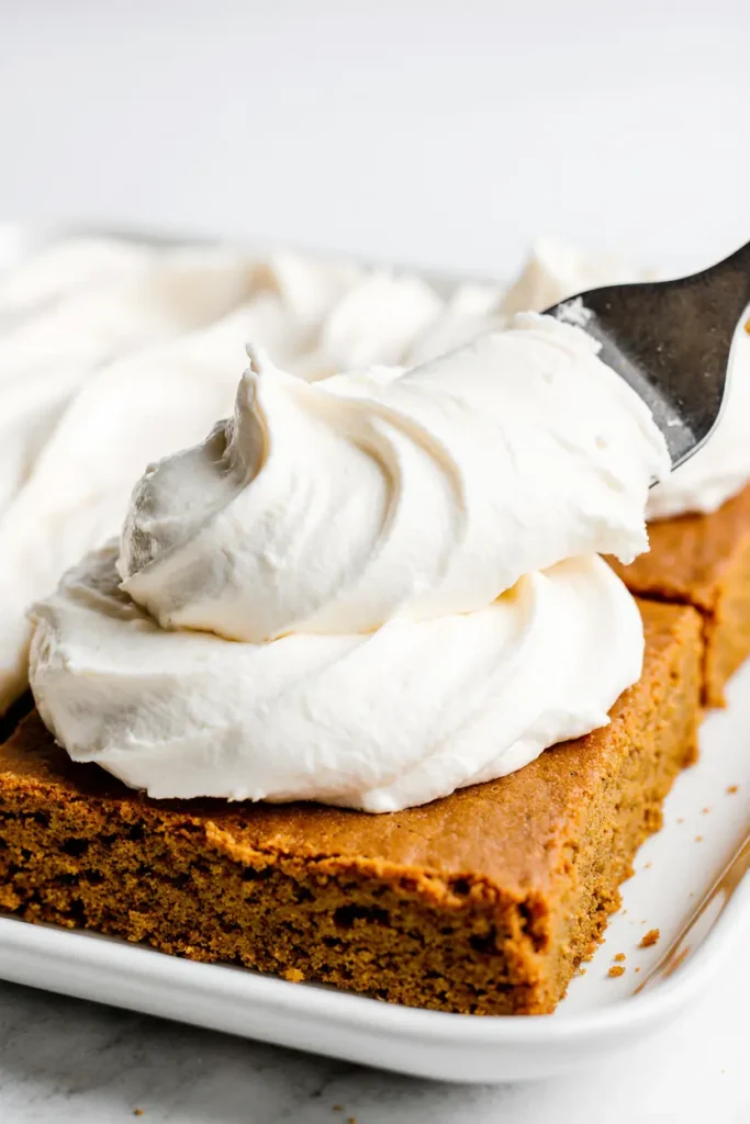 Spreading thick cream cheese frosting over soft pumpkin bars with an offset spatula.