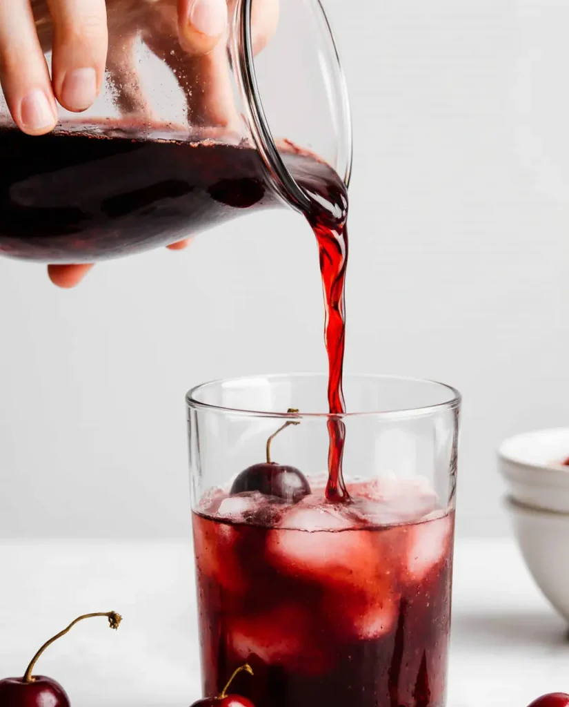 making-cherry-cream-soda-syrup Pouring homemade cherry syrup into a glass to make the cherry cream soda recipe.