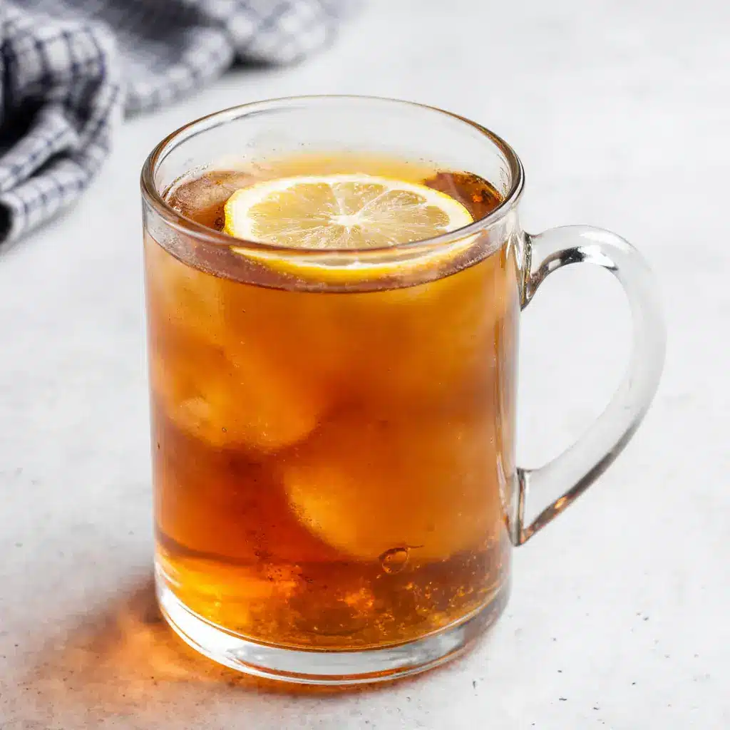 Clear glass mug filled with warm gelatin tonic drink with lemon slice and steam rising